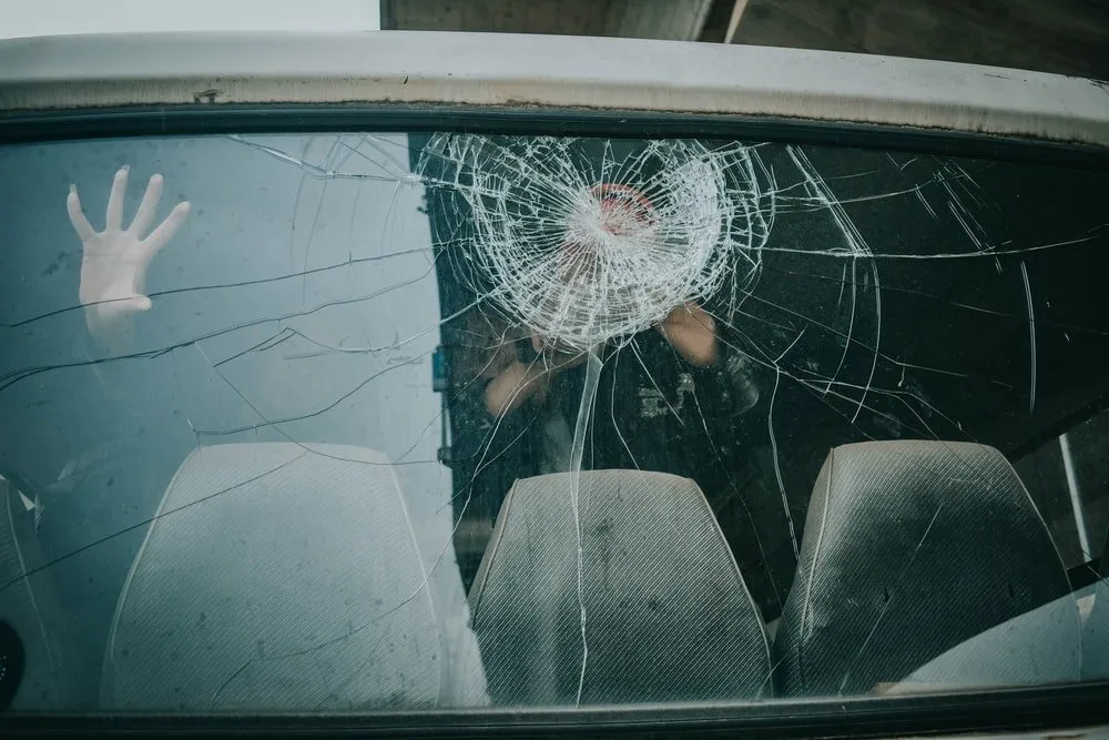 person inside car touching a cracked windshield